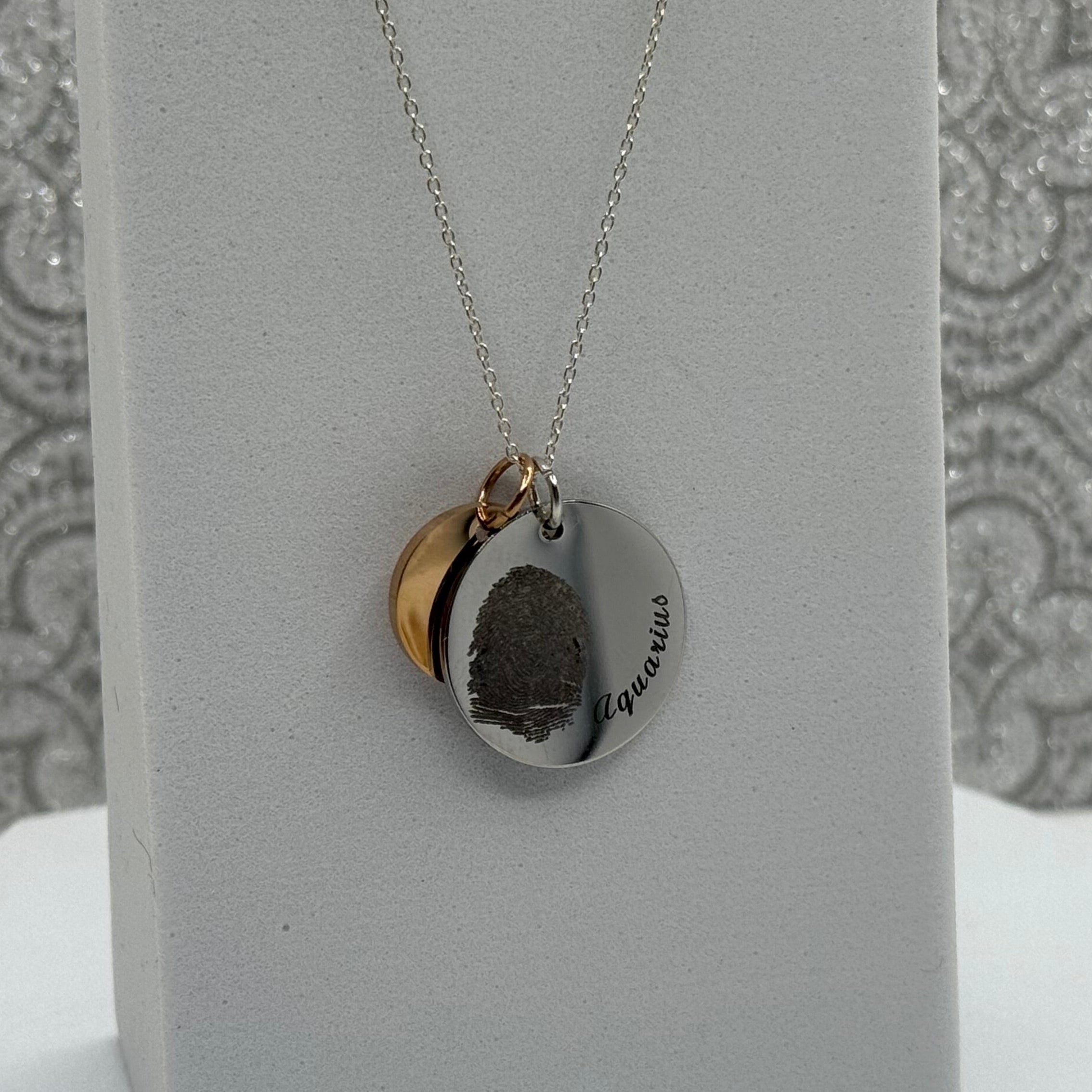 19mm Disc Pendant in Stainless Steel with a fingerprint and Aquarius curved along the edge. It is paired with a 13mm Rose Gold Coated Stainless Steel Disc that can also be engraved with Initials or a small design of your choice. Above the necklace is 3 Angel Wing Charms we offer in Stainless Steel, Gold Coated Stainless Steel, and Rose Gold Coated Stainless Steel.
